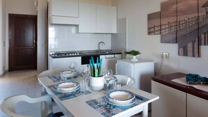 A modern kitchen with white cabinets, a stove, and a sink. There is a dining table set with plates, glasses, and a plant. - Casa della Luna - One Bedroom Apartment, Sleeps 3 (Agrustos)