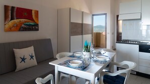 A dining area with a table set for two, a sofa with a star pillow, and a kitchen with a gas stove. - Casa della Luna - One Bedroom Apartment, Sleeps 3 (Agrustos)
