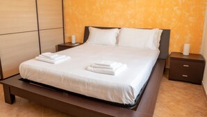 A neatly made bed with white linens and two folded towels, a wooden nightstand with a lamp, and a dark wooden bench at the foot of the bed. - L'Alzoni - Two Bedroom House, Sleeps 5 (L'alzoni)