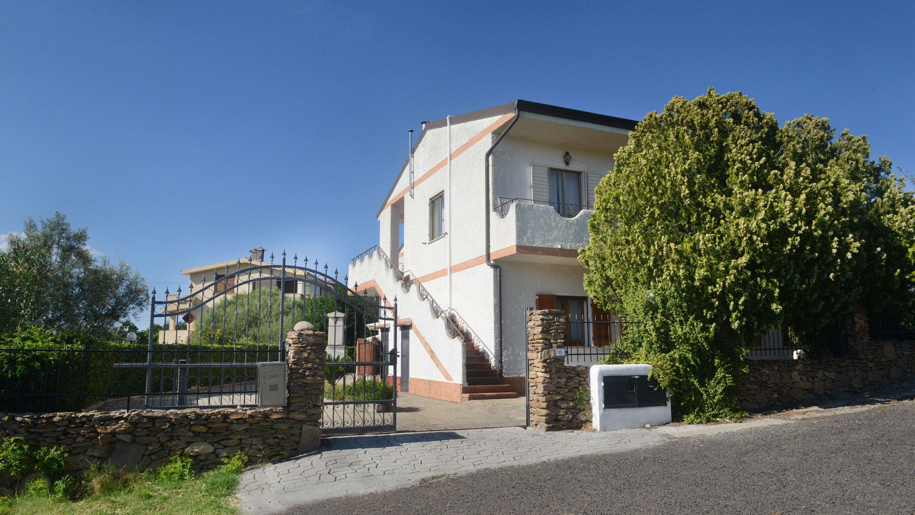 A two-story house with a stone entrance, a staircase, and a large tree in front.