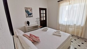 A hotel room with a bed, a small desk, a chair, a door, and a window with curtains.