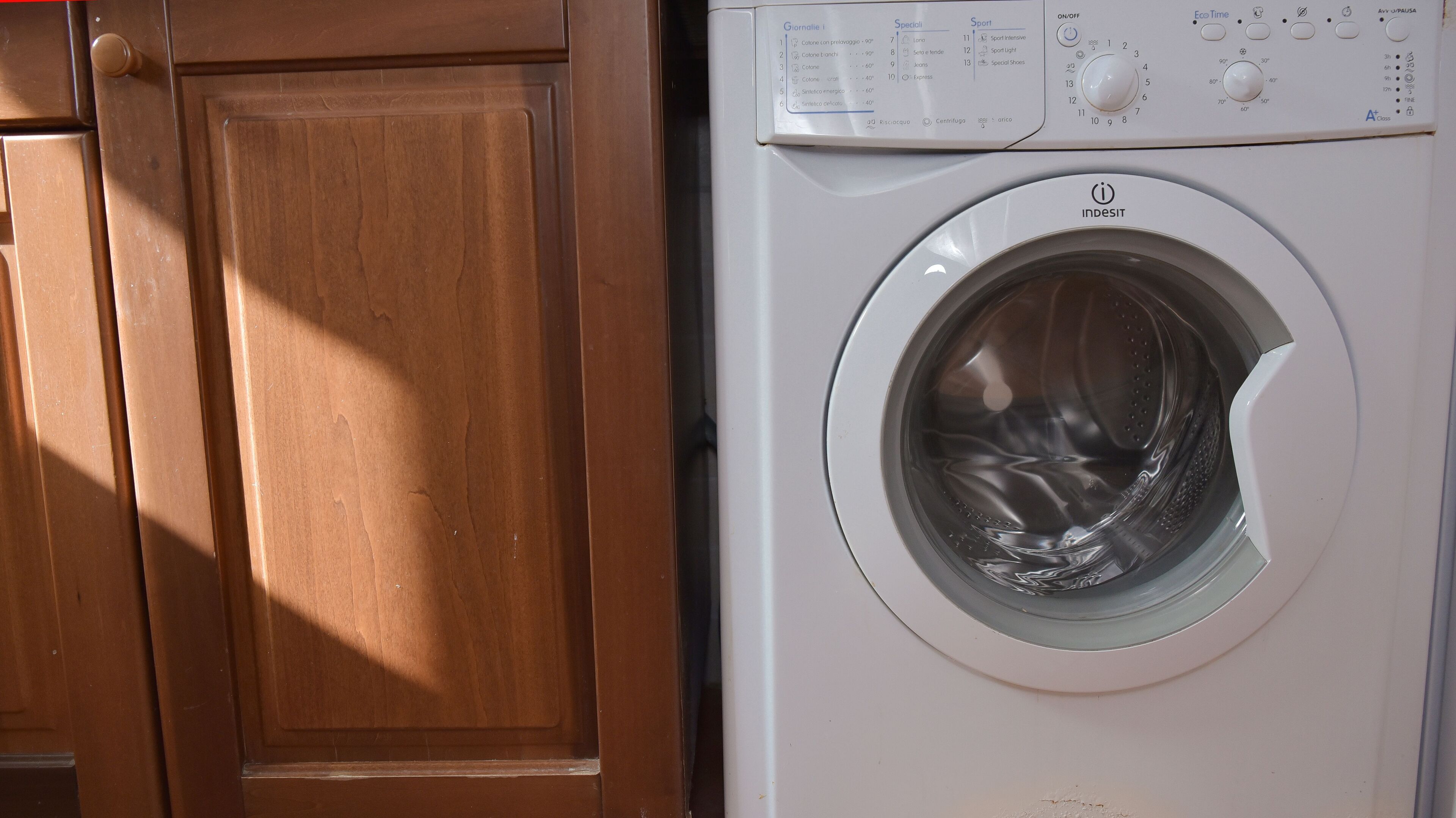 Une vue de face d’un lave-linge blanc, doté d’un panneau de commande, placé à côté d’une porte en bois.
