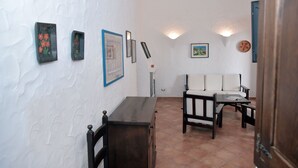 Una habitación con pared blanca con textura, un escritorio de madera, un sofá y piso de baldosas.