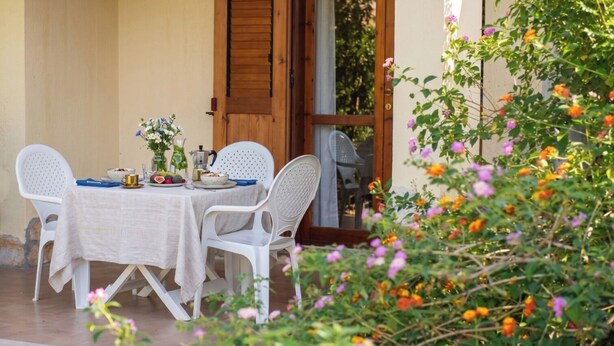An outdoor dining area with a table set for two, surrounded by white plastic chairs.