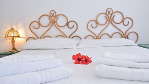A neatly made bed with white linens, a decorative headboard, and a single red flower.