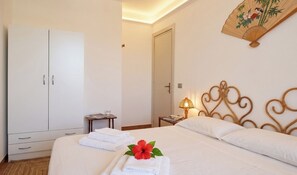 Ein Hotelzimmer mit Bett, Kleiderschrank, Nachttisch mit Lampe und einem Wandventilator.