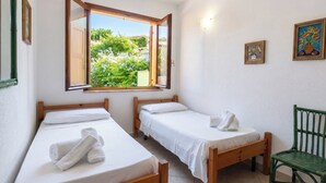 A room with two single beds, a window with a view of greenery, and a green chair. - Villa Giorgia with garden - 50m from the Beach (Costa Rei)