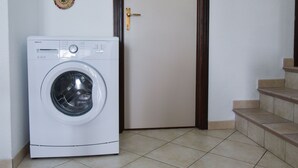 A front-loading washing machine in a room with a tiled floor and a wooden door. - Villa Giorgia with garden - 50m from the Beach (Costa Rei)