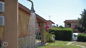 A showerhead with water flowing, a house with a stone facade, and a vehicle parked in the background. - Villa Oleandro with garden & BBQ - near the beach (Costa Rei)