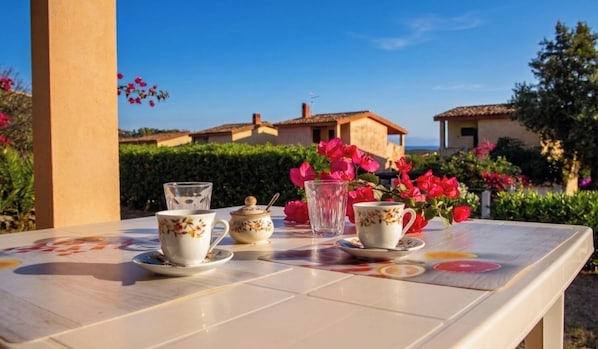 Una mesa con tetera, tazas y platos, dispuesta al aire libre con vistas a edificios y vegetación.