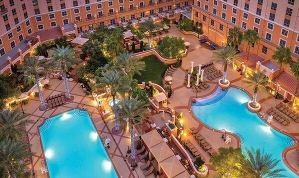 Two pools surrounded by palm trees and lounge areas in a tranquil courtyard setting.