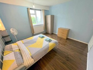 Une chambre à coucher comprenant un lit, une armoire, une table de chevet, un ventilateur et une fenêtre avec des rideaux.