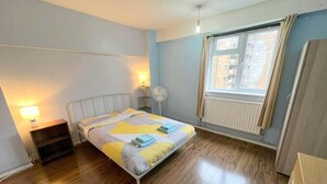 Ett sovrum med en säng, sänglampor, ett element och ett fönster med gardiner.