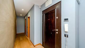 A hallway with wooden flooring, a dark wooden door, a wall-mounted telephone, and a light switch.