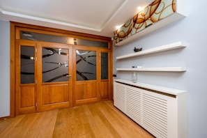 Een gang met houten dubbele deuren, witte planken en een witte radiator.