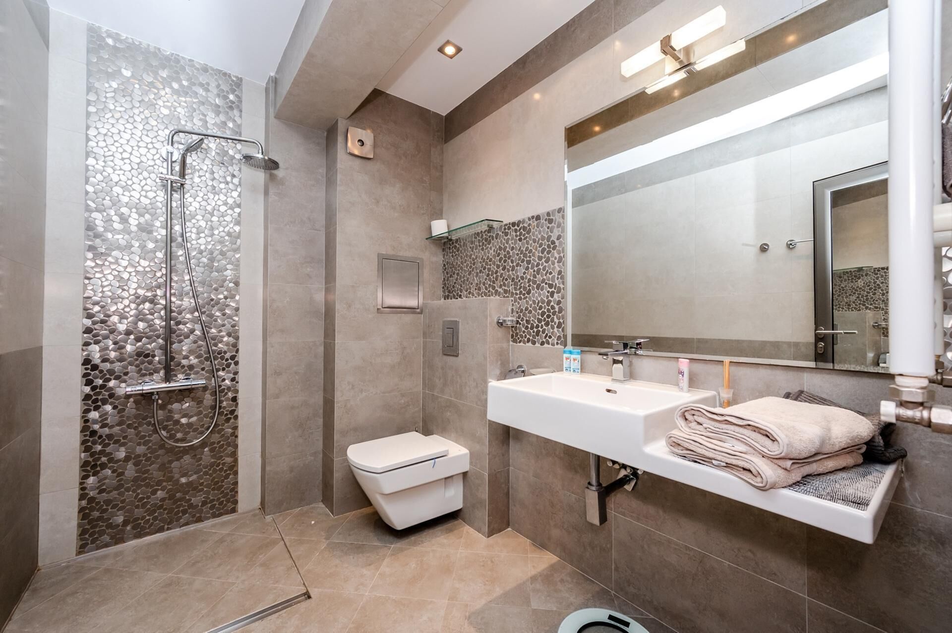 A modern bathroom with a shower, toilet, and vanity with a large mirror.