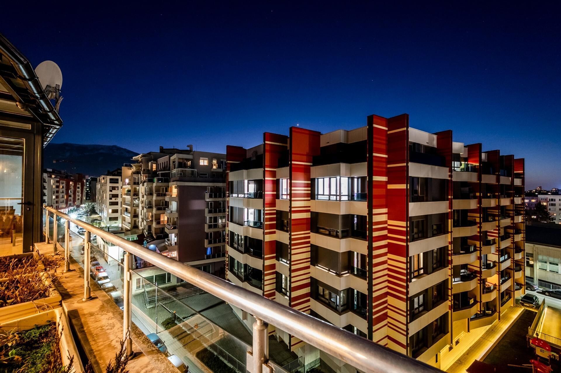 Un edificio de varios pisos con balcones, barandilla de vidrio y vista de la calle.