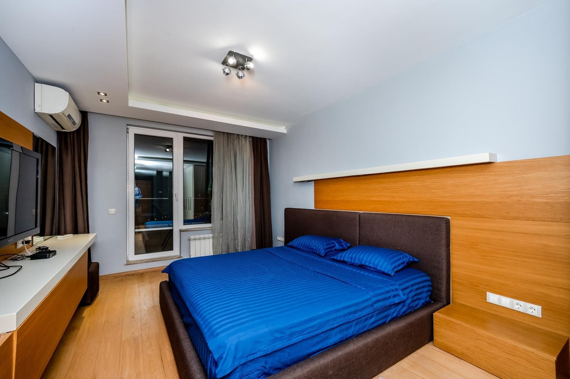 Una habitació d'hotel amb un llit, televisió, escriptori i finestra amb cortines.