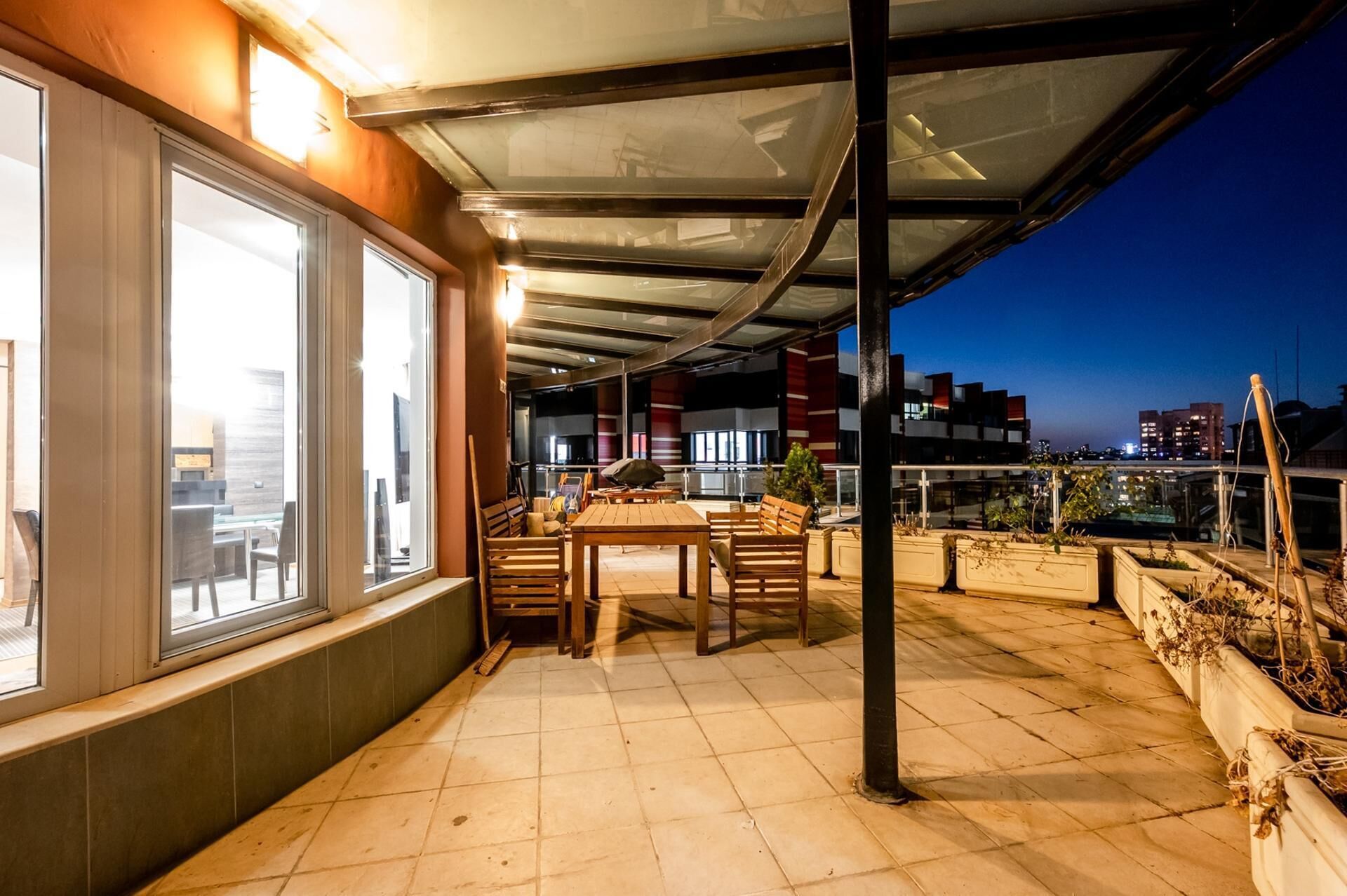 An outdoor patio area with a table and chairs, a covered seating area, and a view of the cityscape at dusk.