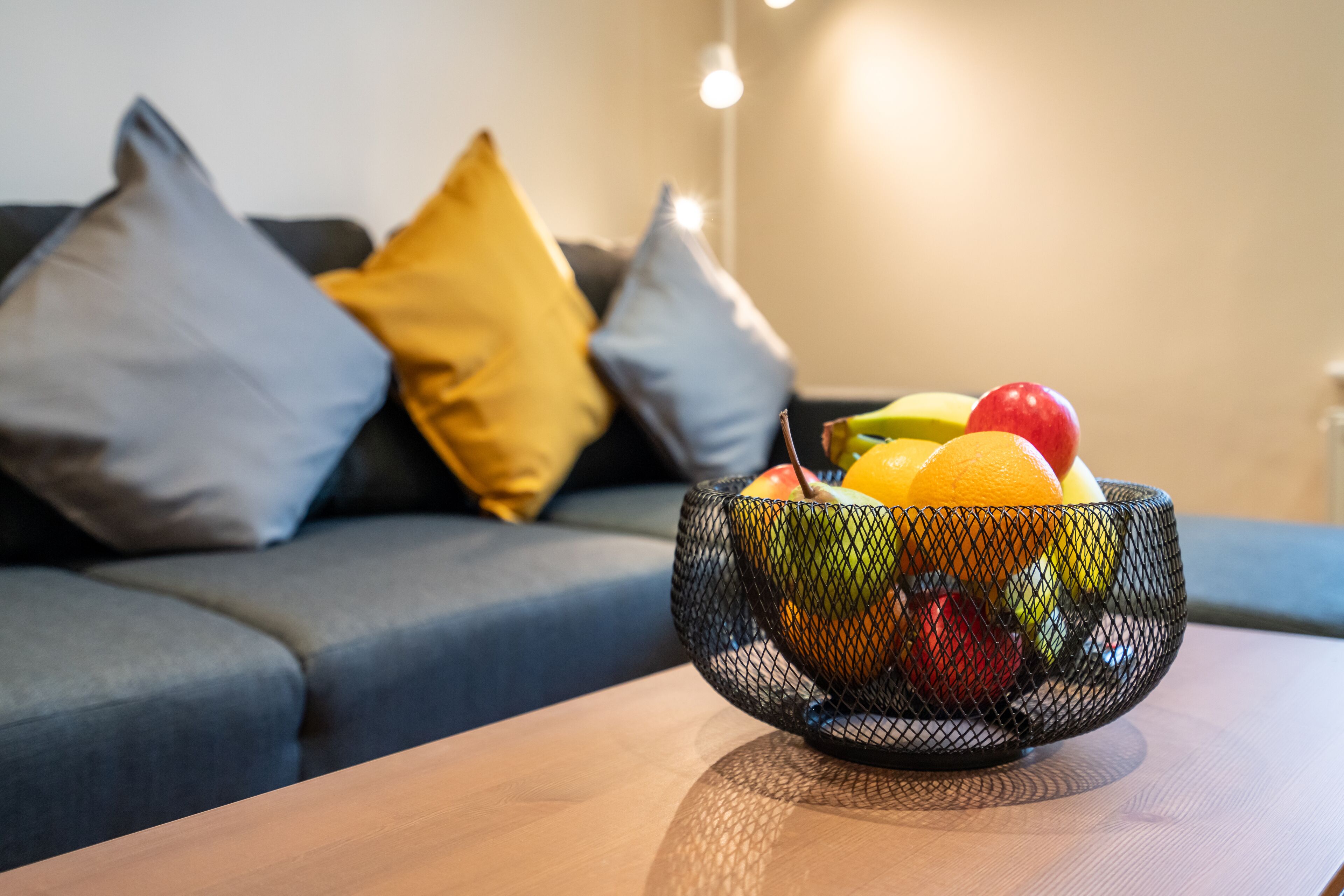 Eine Obstschale auf einem Tisch, im Hintergrund ein Sofa und Kissen.