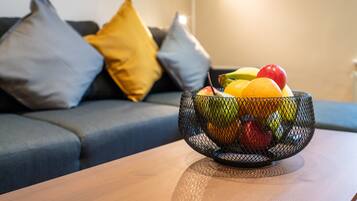 A fruit bowl on a table with a sofa and cushions in the background.