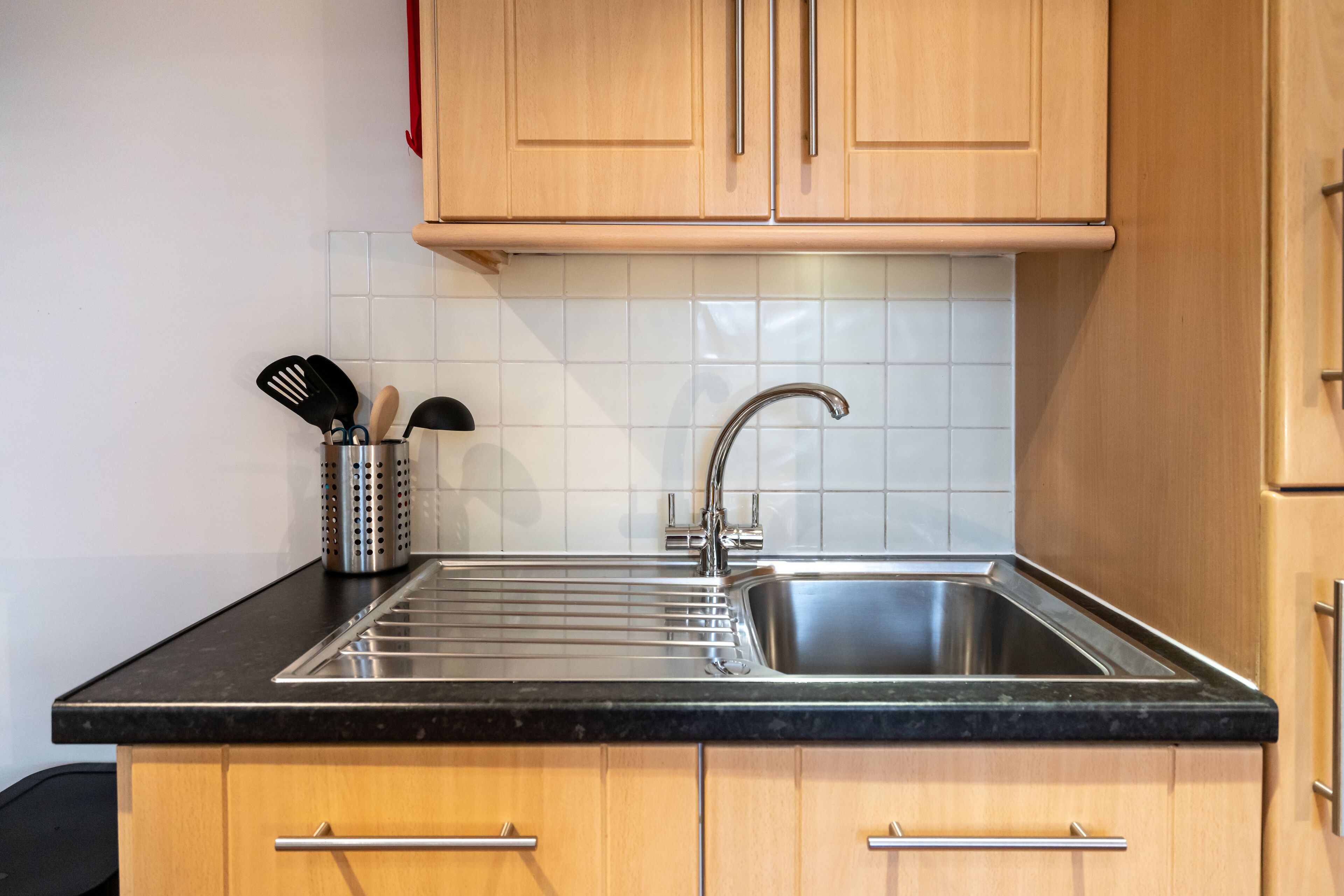A kitchen with wooden cabinets, a stainless steel sink, and a black countertop.