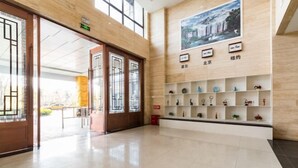 A hotel lobby with a wooden floor, a reception desk, and a wall with shelves displaying various items. - ELONG ruiyun Hotel (Yancheng International Exhibition Center) (Yancheng)