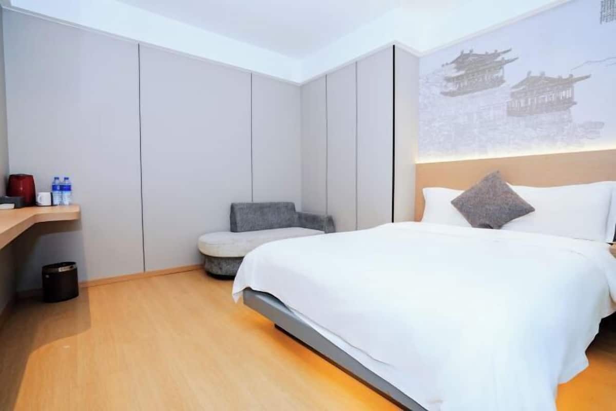Ein Hotelzimmer mit Bett, einem Sessel, einem kleinen Tisch mit Wasserflaschen und einer Wand, auf der traditionelle Architektur projiziert wird.