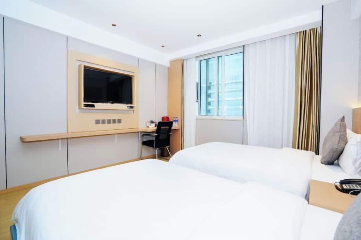 Ein Hotelzimmer mit Bett, Schreibtisch, Stuhl, Fernseher und einem Fenster mit Vorhängen.