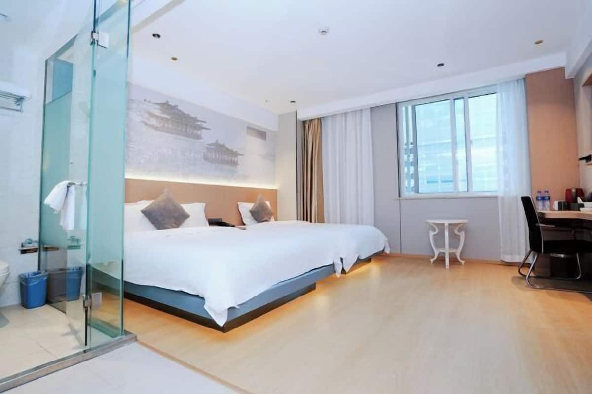 Ein modernes Hotelzimmer mit einem großen Bett, einer Dusche mit Glastrennwand, einem kleinen Tisch und einem Schreibtisch mit Stühlen.