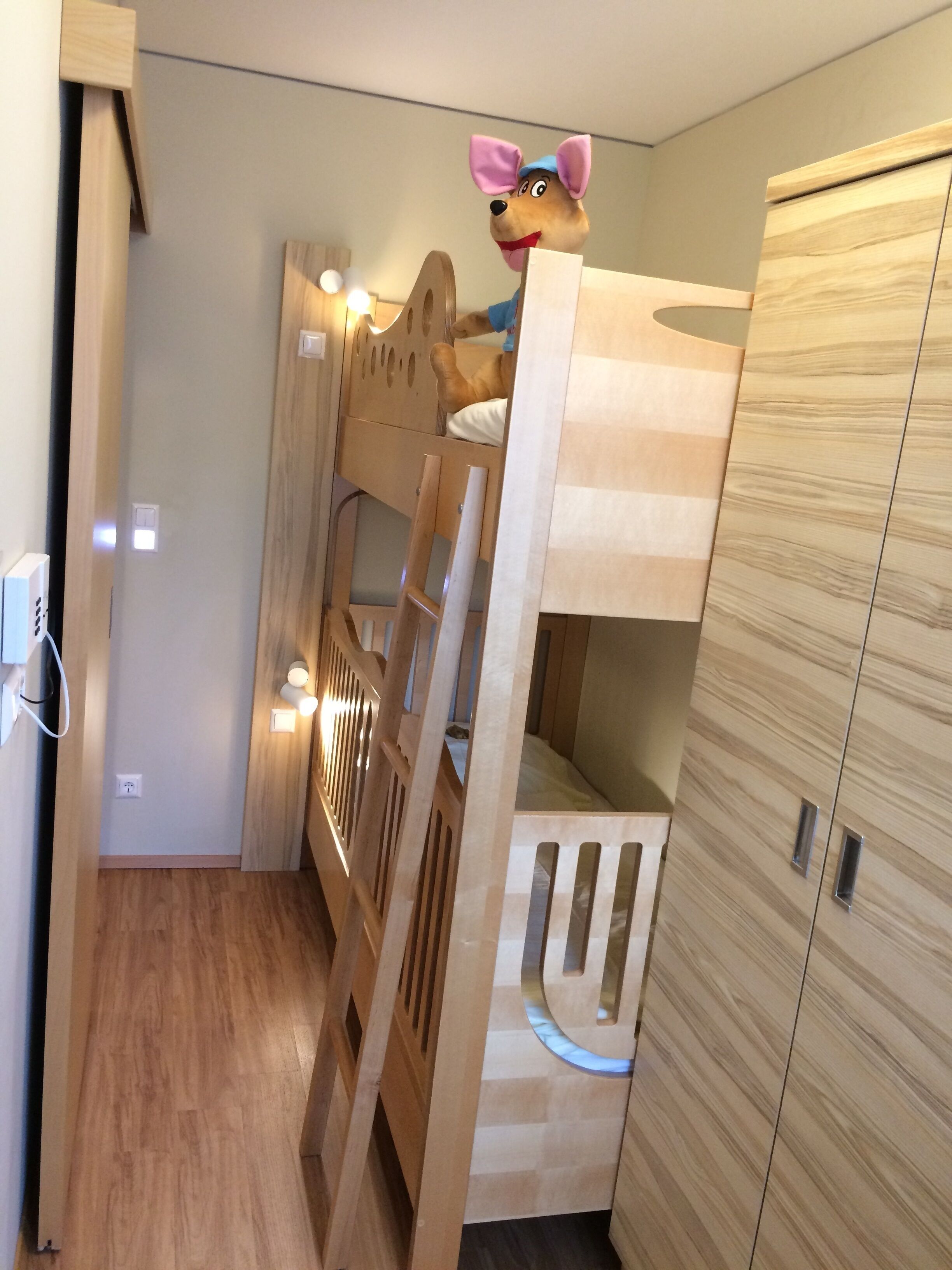 Ein Etagenbett mit Holz Kopfteil, ein Kleiderschrank mit Spiegel und eine Steckdose.