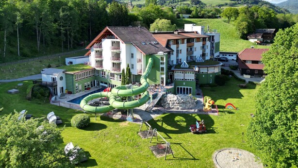 Un hotel con un tobogán acuático verde, varias construcciones y montañas al fondo.