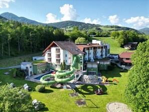Un hotel con un tobogán acuático verde, varias construcciones y montañas al fondo.