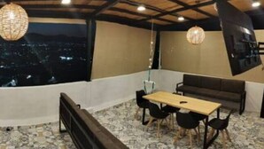 A balcony with a city view, a table with chairs, a sofa, and a hanging light fixture.