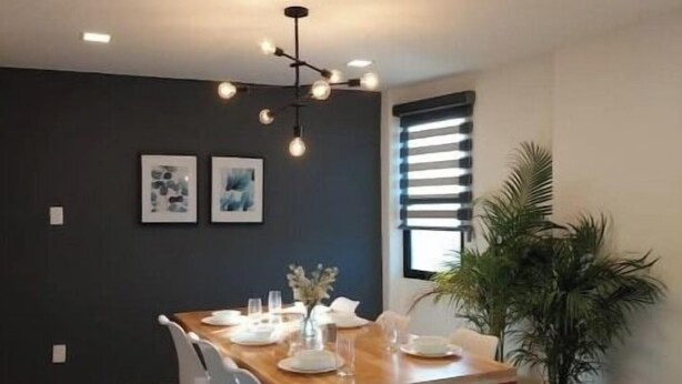 A modern dining area with a wooden table set for six, surrounded by white chairs.
