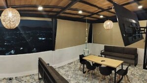 A room with a curved wall, a dining table, chairs, a sofa, and a large window overlooking a cityscape at night.