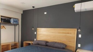 A bedroom with a large bed, wooden headboard, two bedside tables, a wardrobe, and a hanging light fixture.