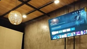 Ein Konferenzraum mit einer großen Leinwand, die eine Präsentation zeigt, einem Holztisch, schwarzen Stühlen und einem gemusterten Teppich.