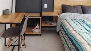 Ein gemütliches Schlafzimmer mit Bett, Schreibtisch und Stuhl. Ein Regal mit Kleidern und einer kleinen Aufbewahrungsbox.