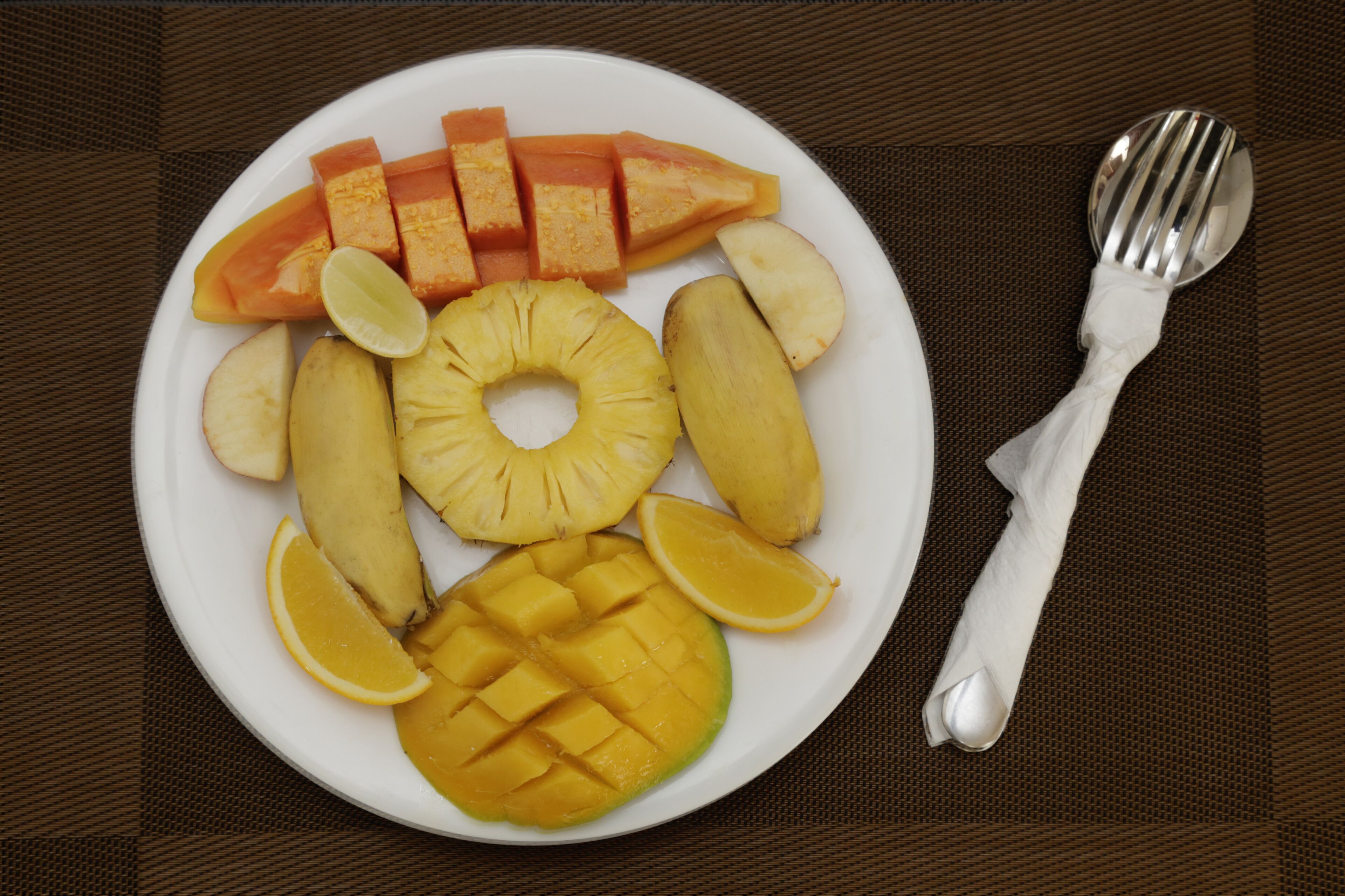 A plate of fruit including pineapple, mango, and orange slices, with a fork beside it.