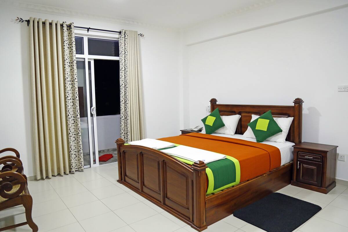 A neatly arranged bedroom with a wooden bed, a small bedside table, a chair, and a window with curtains.