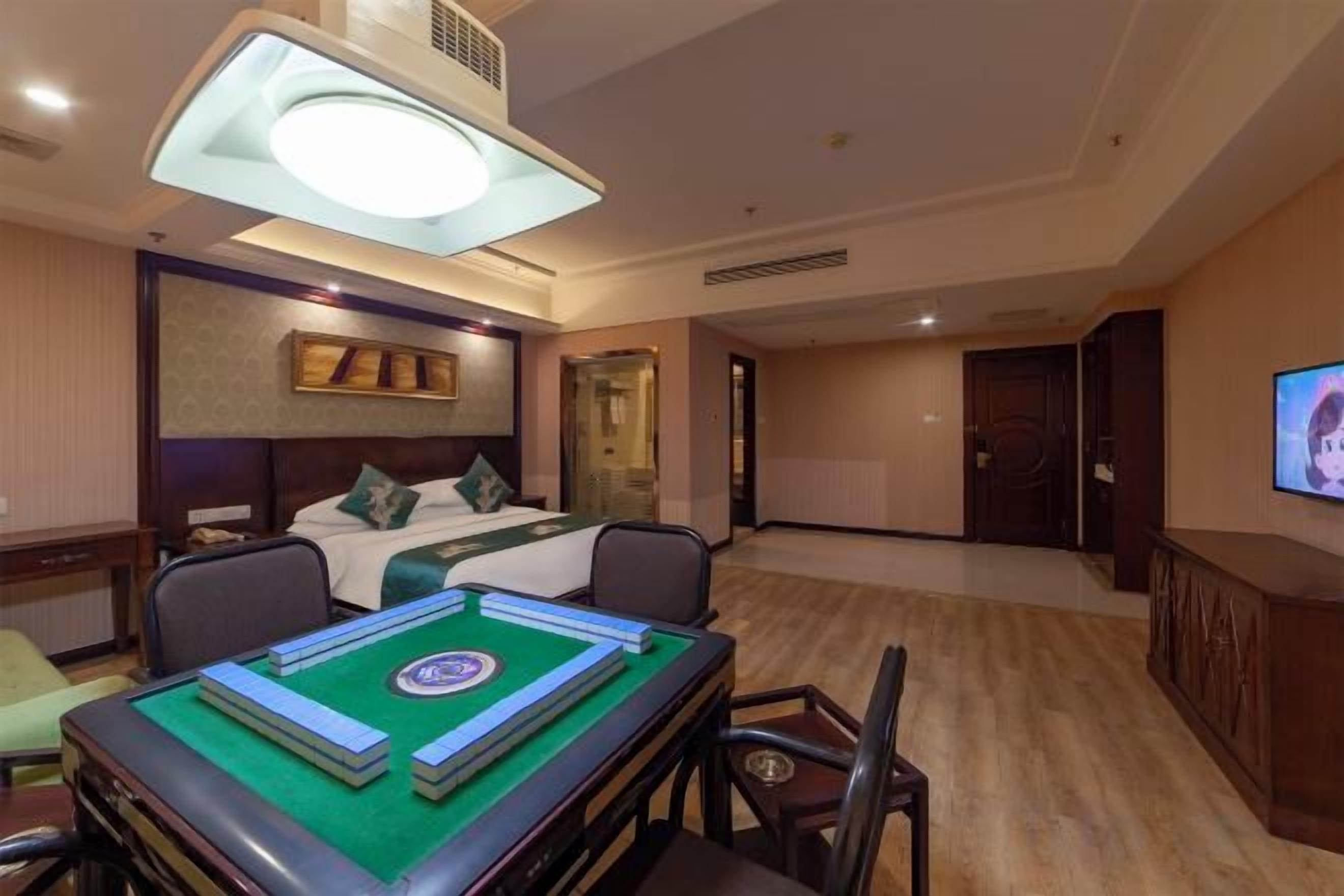 A hotel room with a bed, a desk with a board game, a television, and a large window.