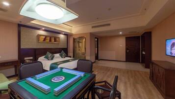 A hotel room with a bed, a desk with a board game, a television, and a large window.
