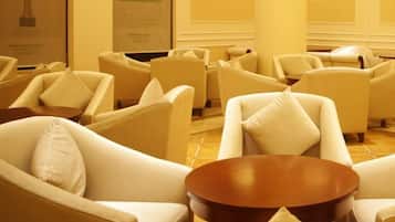 A hotel lounge with multiple white armchairs and a central wooden coffee table.