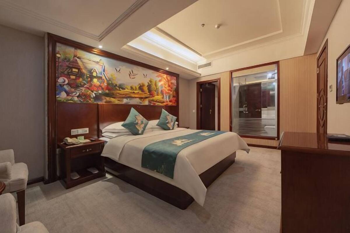 Habitación de hotel con una cama grande, una mesita de noche, un escritorio, una silla, un cuadro en la pared y una puerta corredera.