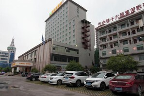 A hotel with multiple floors, a parking lot with several cars, and a flag on the building. - Vienna Hotel ( Hunan Zhangjiajie City Park ) (Zhangjiajie)