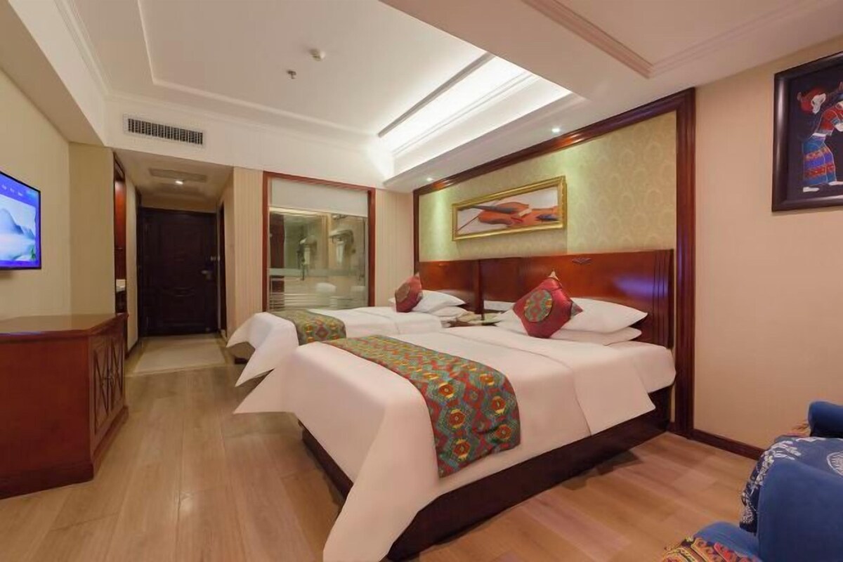 A hotel room with a bed, a desk, a television, and a painting on the wall.