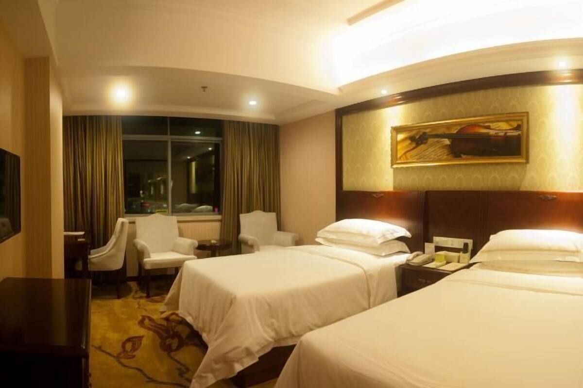 Una habitación de hotel con dos camas, un escritorio, una silla, un televisor y una ventana con cortinas.