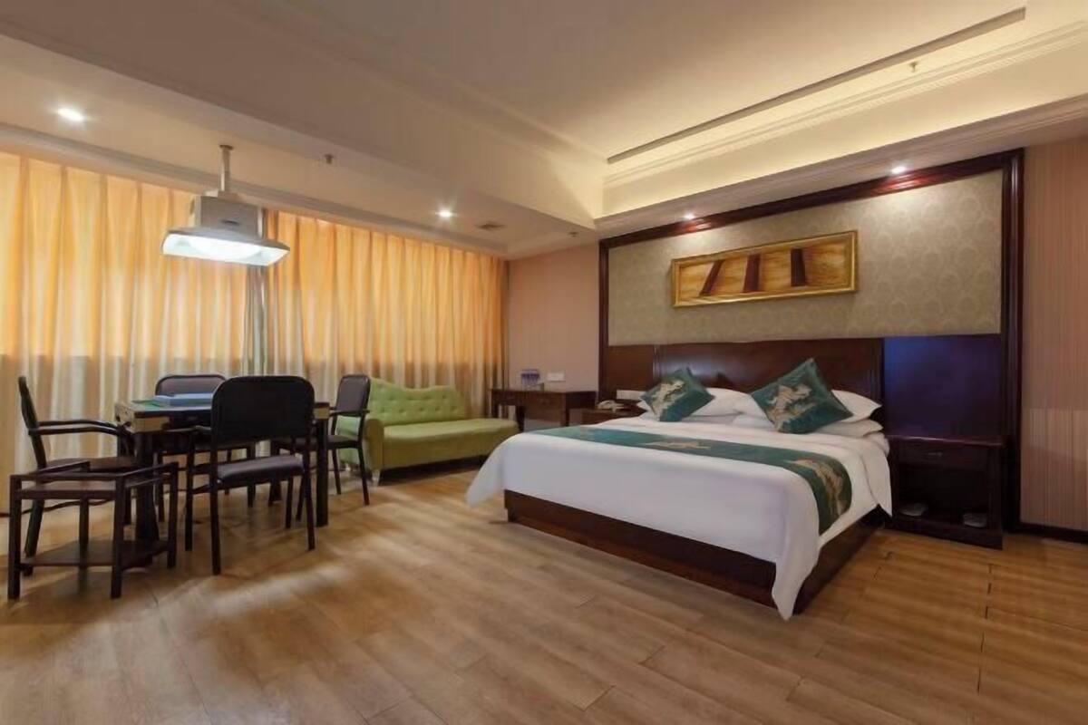 Una habitación de hotel con cama, escritorio, sillas, lámpara y ventana con cortinas.