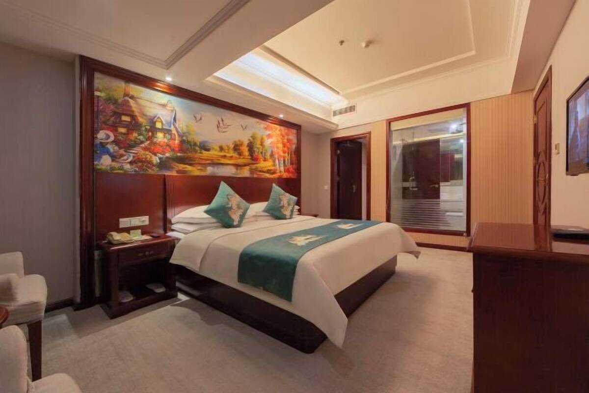 Habitación de hotel con una cama grande, una mesita de noche, un cuadro en la pared y una puerta corredera que da a un baño.